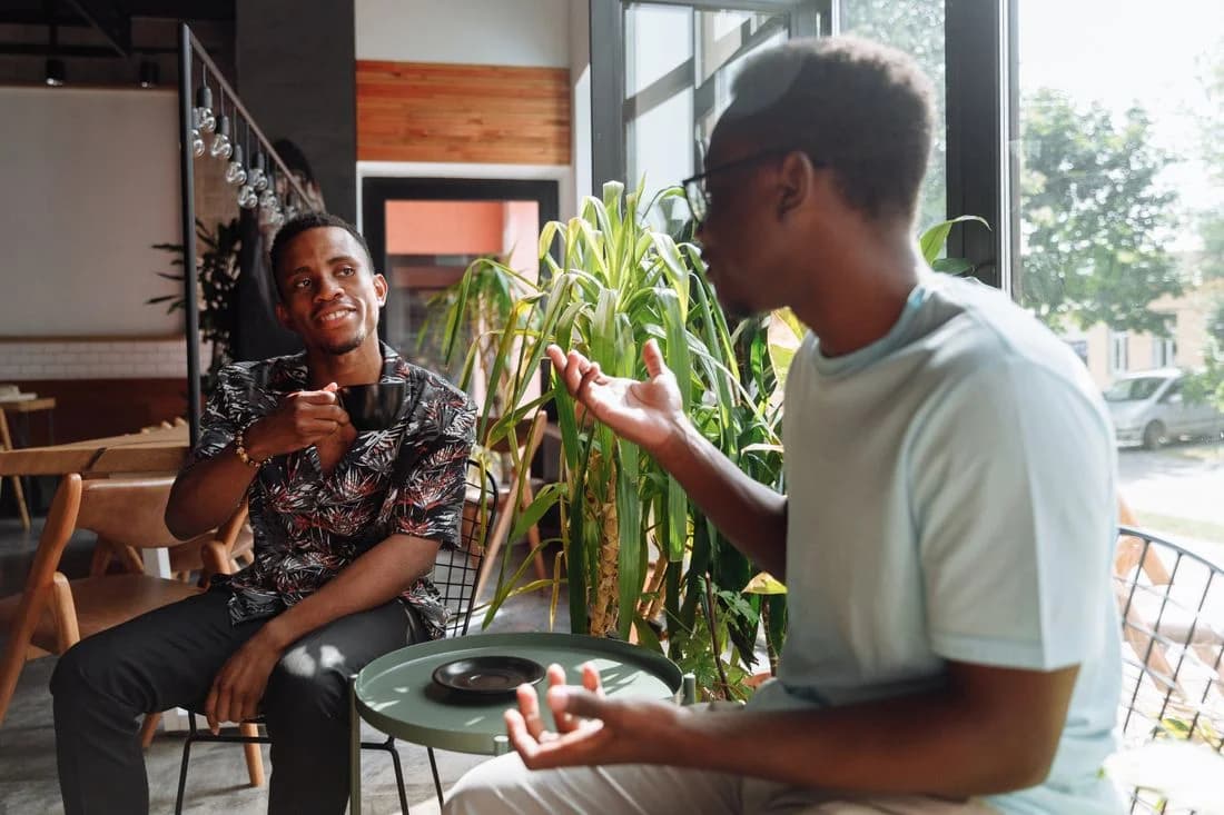 Two friends sharing a conversation in a café beside a sunny window.