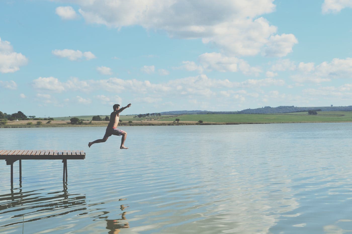A child leaping off a pier into a lake in summer.