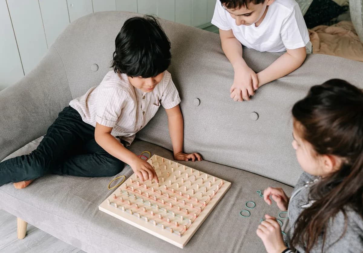 Three children exploring patterns together on a wooden geoboard with colorful elastic bands.