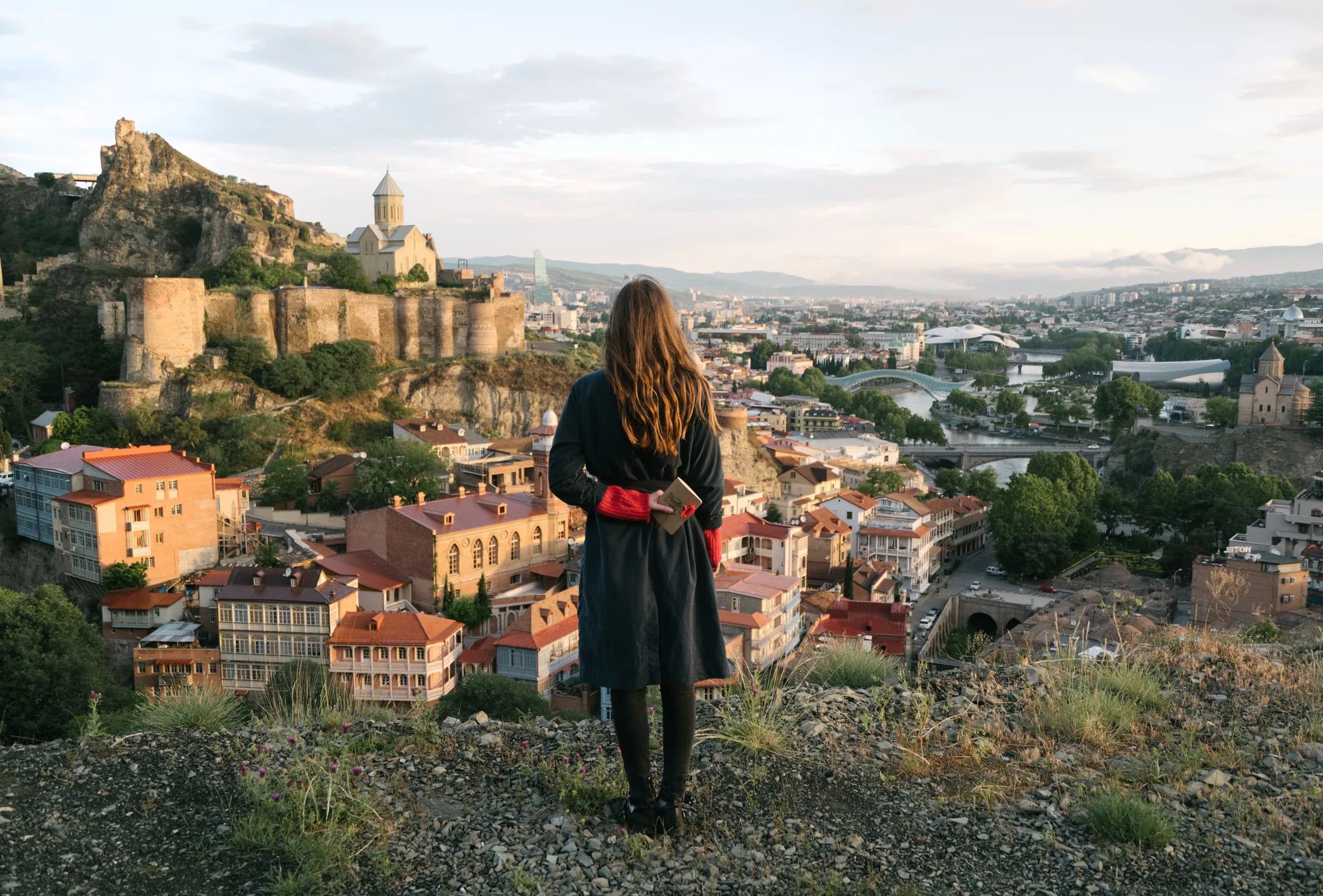 A woman looking out over the old city of Tbilisi and its hilltop fortress at golden hour