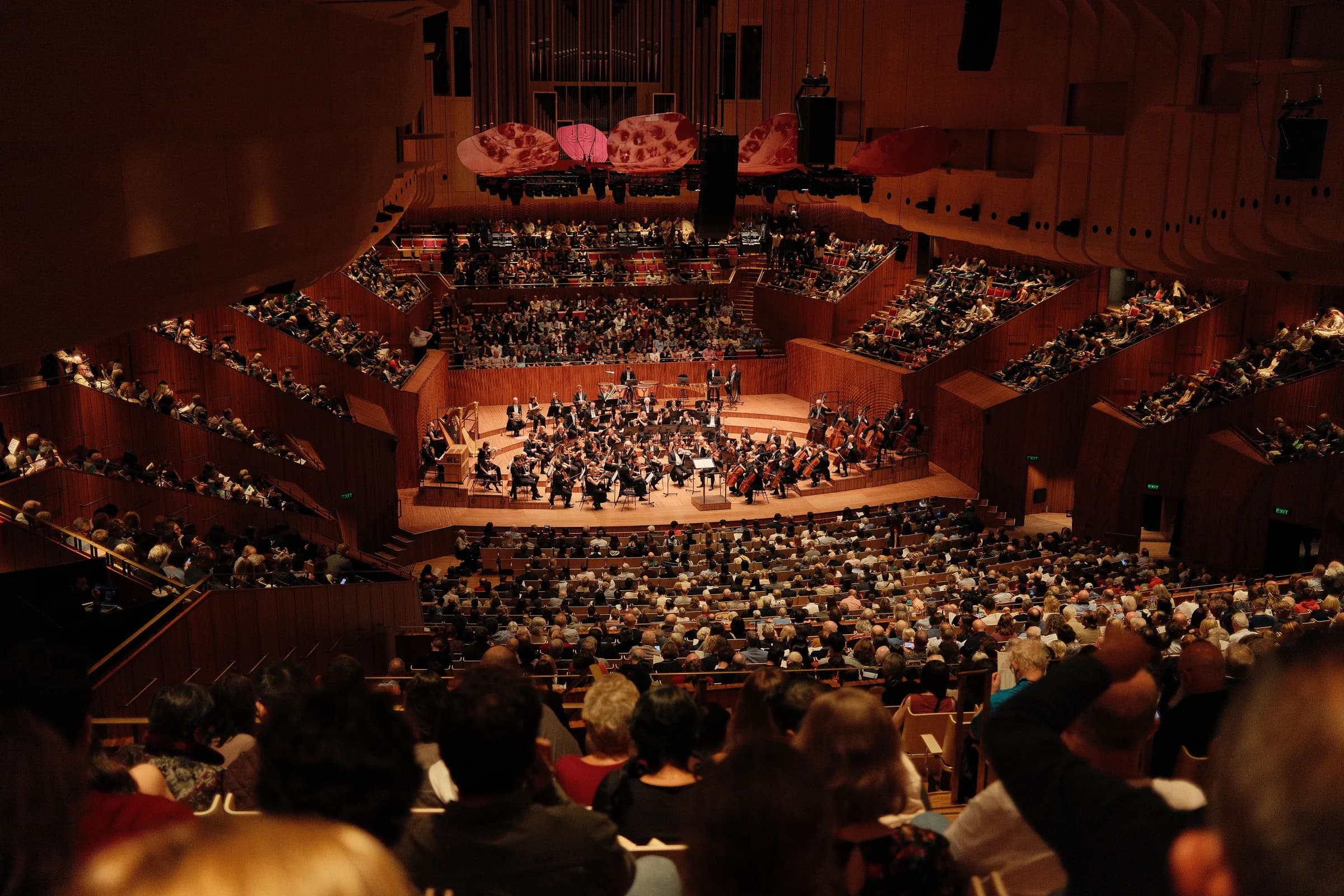 A full concert hall, seen from the back rows, with an orchestra playing on stage