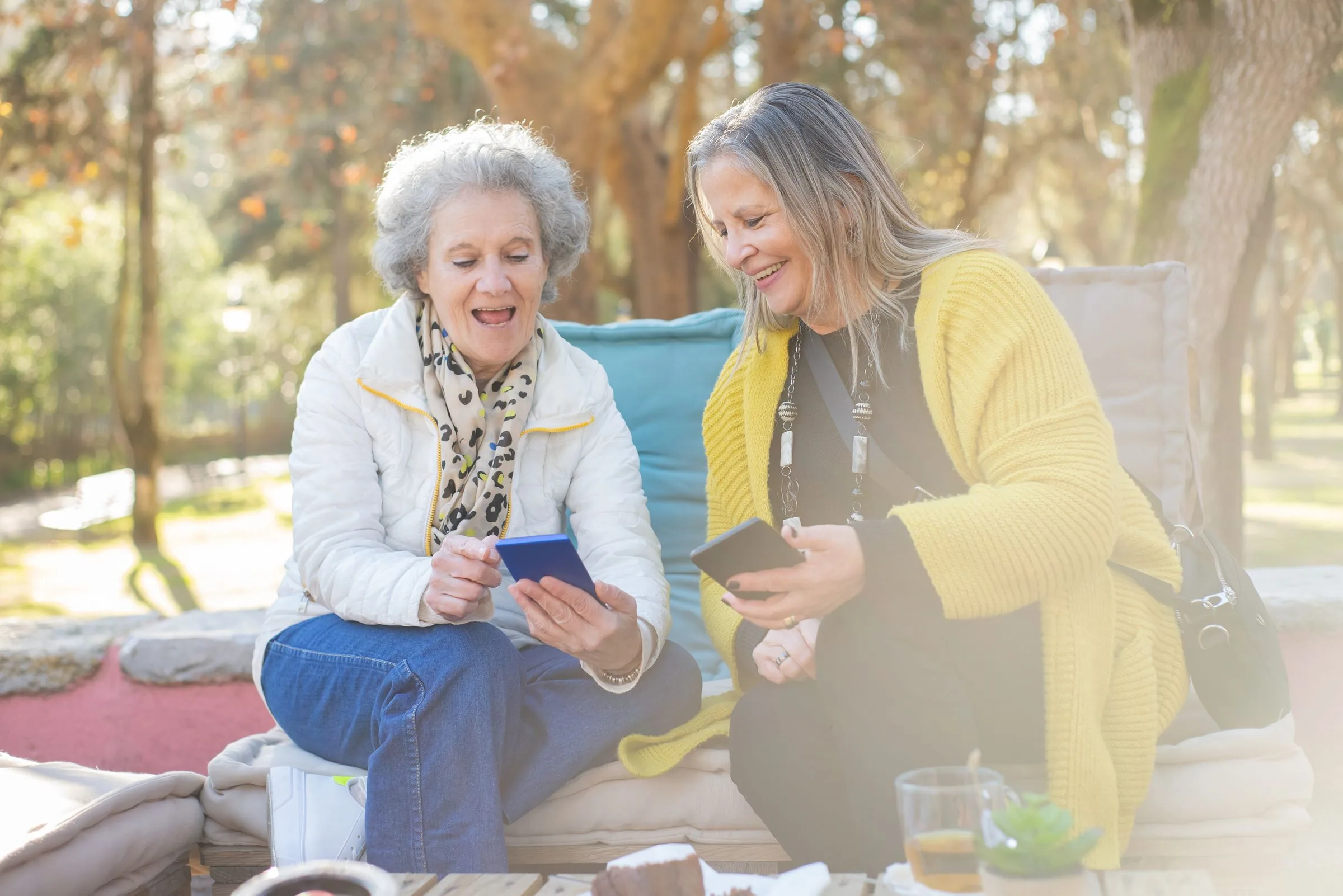 Two older women laughing together on a bench in a sunny park