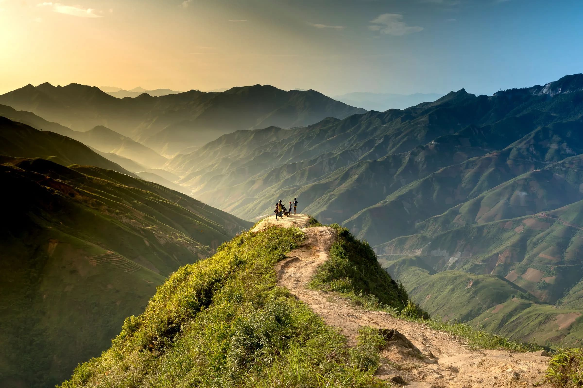 Hikers standing on a green ridge above a mountain range at sunrise