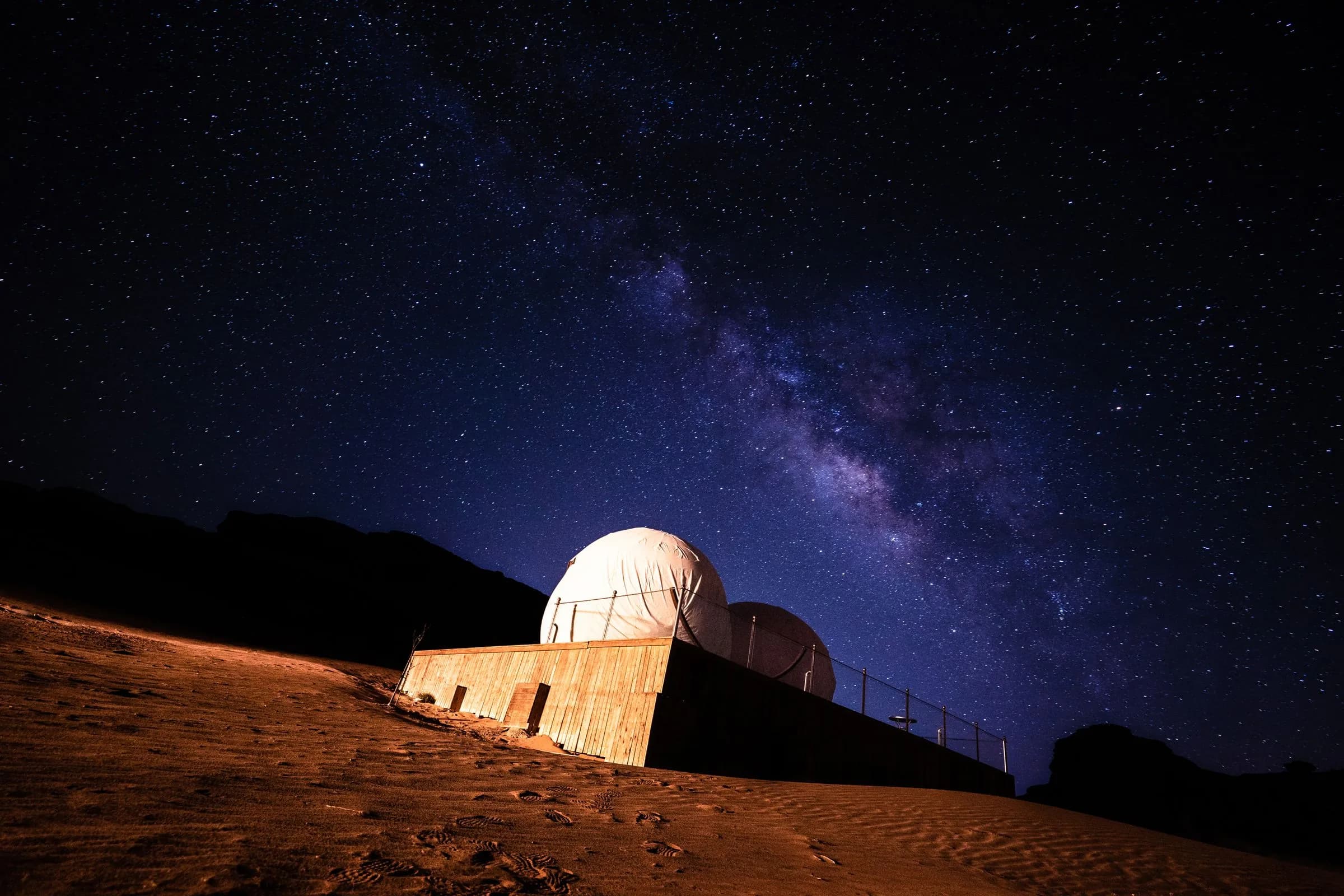 Two white dome tents on a desert slope at night under the Milky Way