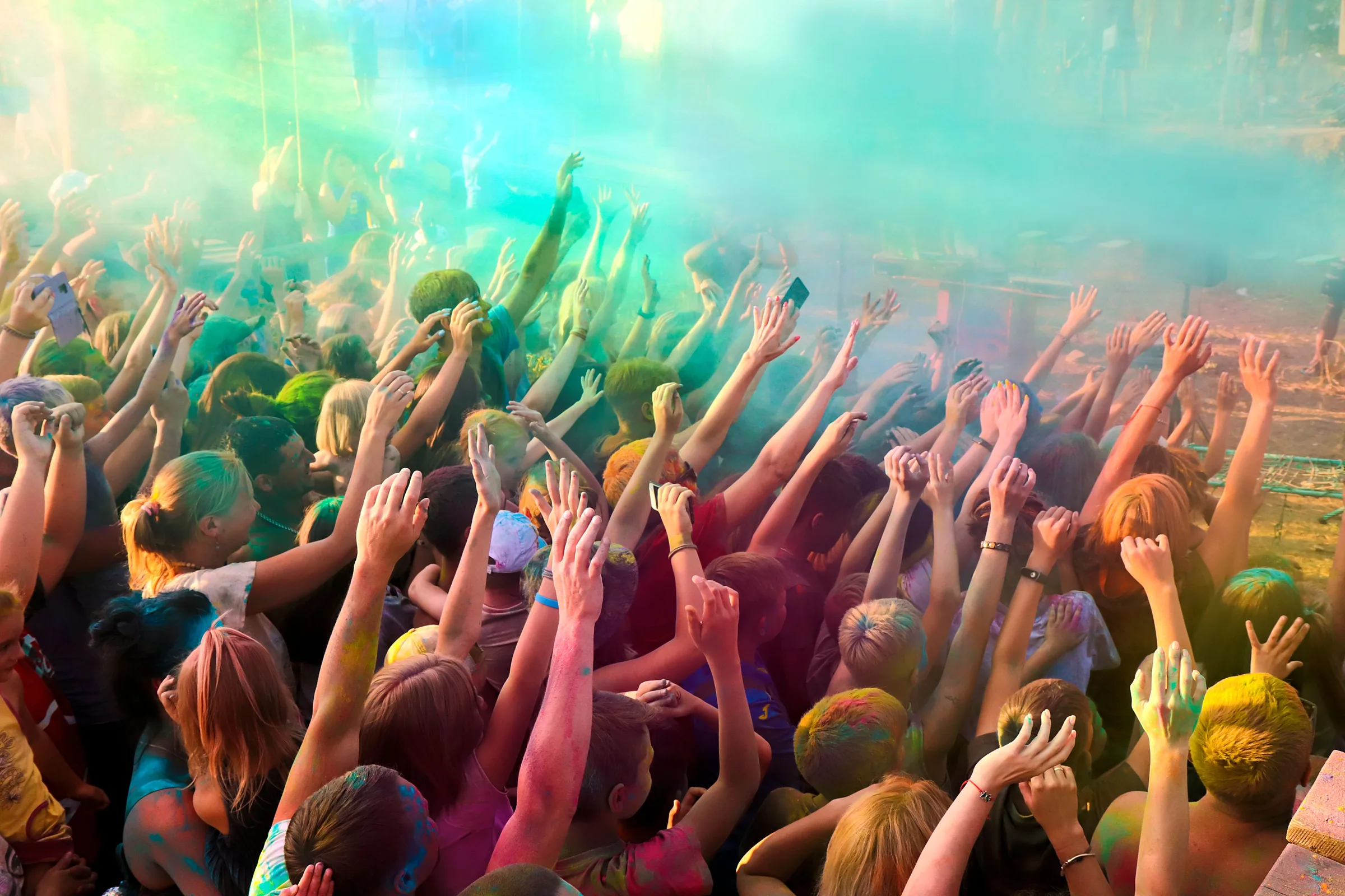 A crowd raising their hands together in a cloud of colored powder
