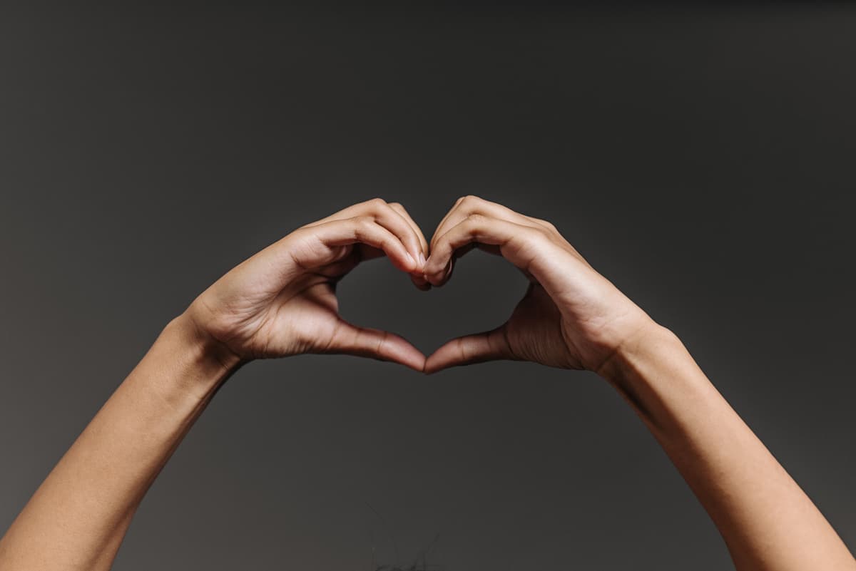 Hands forming a heart shape against a gray background.