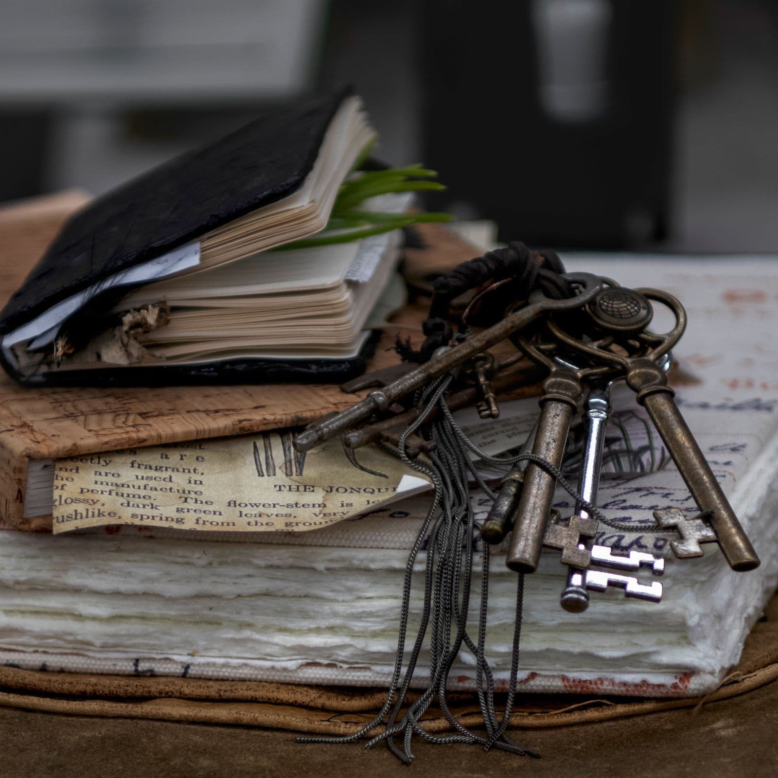 Weathered leather journals stacked beside a cluster of old iron keys on a wooden table.