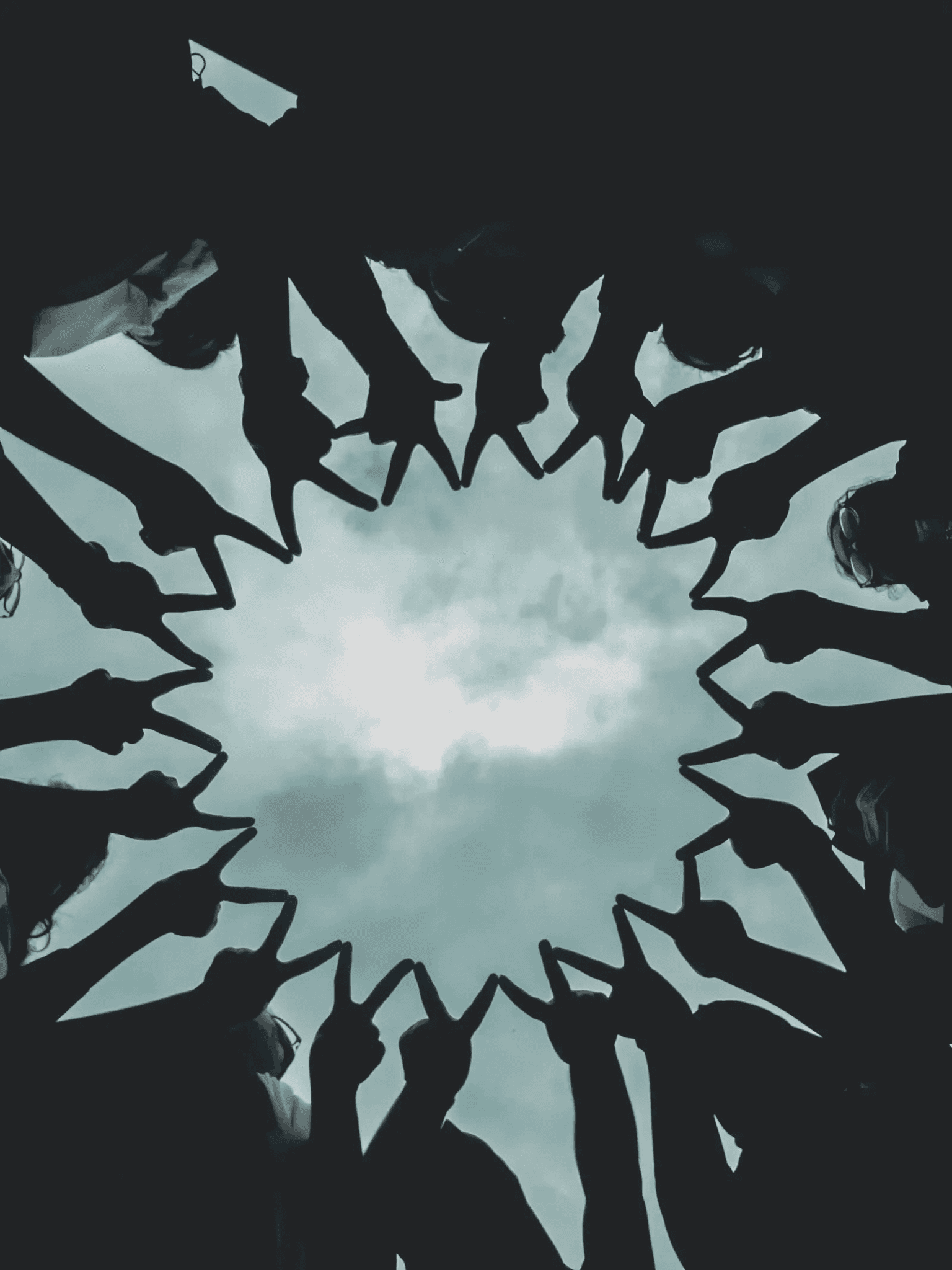 A circle of people joining their hands against the sky.